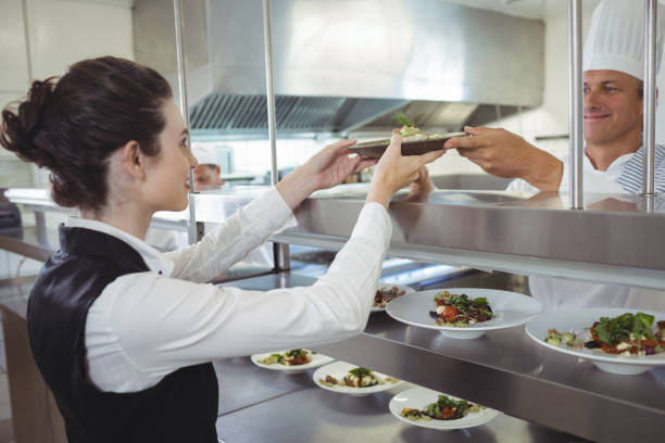 Chef handing food dish to waitress at order station in the commercial kitchen