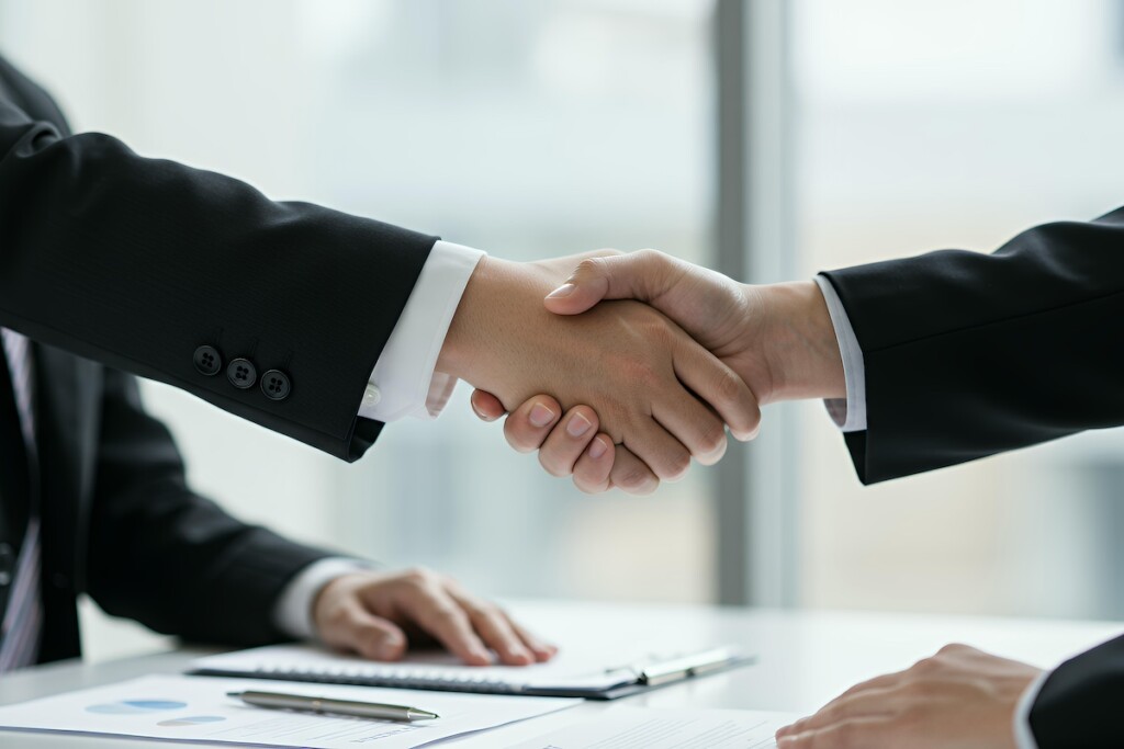 Corporate business handshake agreement between executives with contract documents and pen on professional office desk